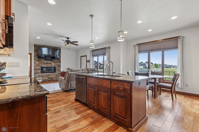 kitchen with pendant lighting, dark stone countertops, a center island with sink, and light hardwood / wood-style flooring