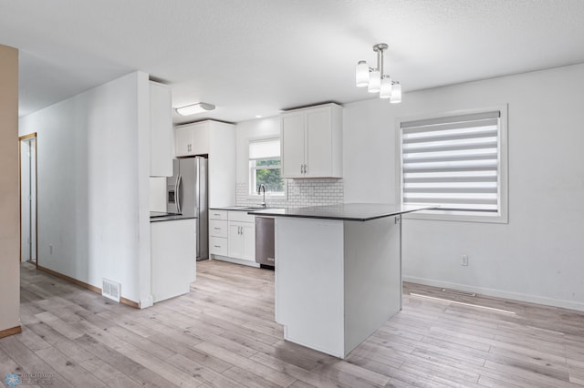 kitchen featuring decorative backsplash, light wood-type flooring, white cabinets, and decorative light fixtures