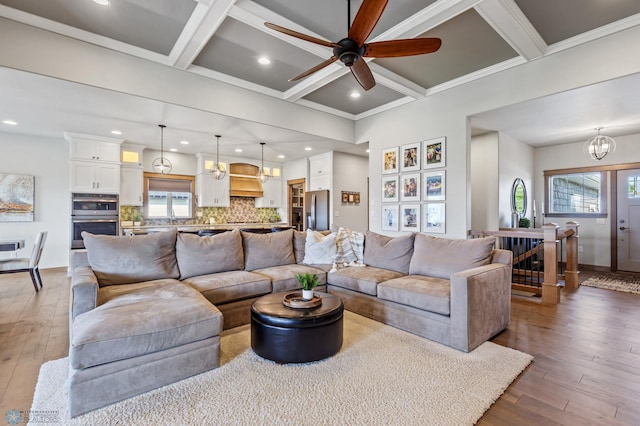 living room with beam ceiling, wood-type flooring, coffered ceiling, and ceiling fan with notable chandelier