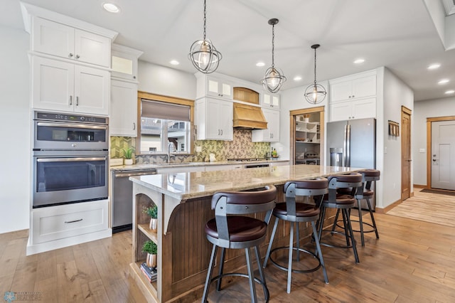 kitchen featuring white cabinetry, stainless steel appliances, decorative backsplash, a center island, and light hardwood / wood-style flooring