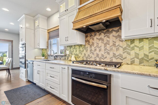 kitchen with tasteful backsplash, a wealth of natural light, light hardwood / wood-style floors, custom exhaust hood, and appliances with stainless steel finishes