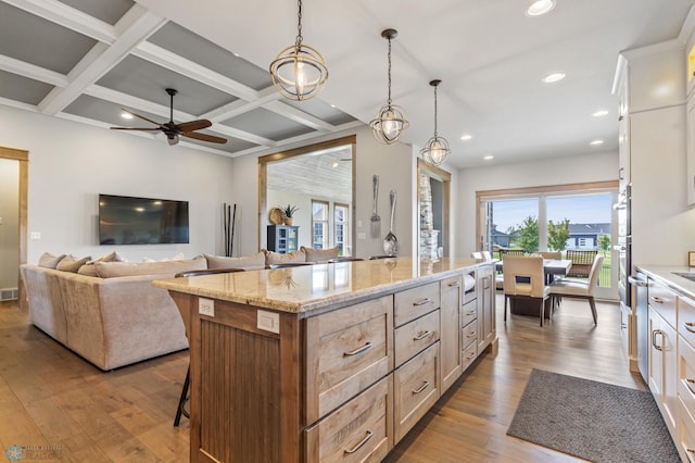 kitchen with light wood-type flooring, a center island, beam ceiling, coffered ceiling, and light stone countertops