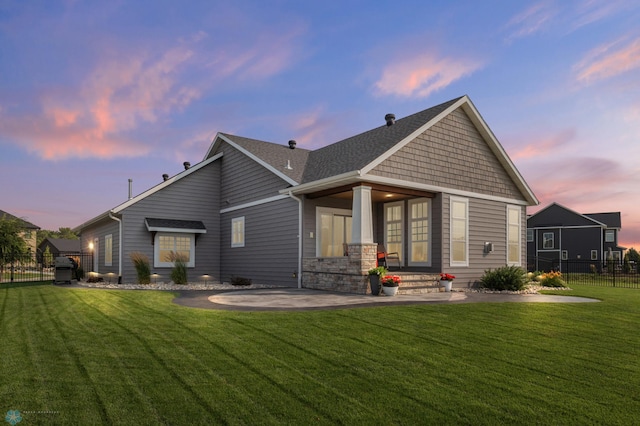 back house at dusk with a patio area and a lawn