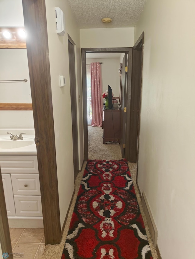 hall with sink, a textured ceiling, and light tile patterned floors