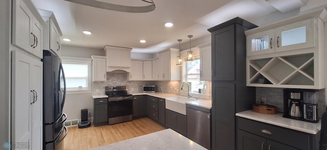 kitchen with appliances with stainless steel finishes, light hardwood / wood-style flooring, white cabinets, sink, and decorative backsplash