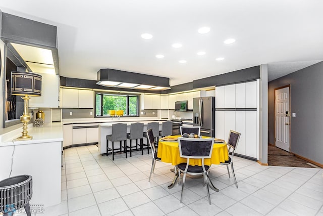 kitchen with light tile patterned flooring, a kitchen bar, white cabinetry, and stainless steel appliances