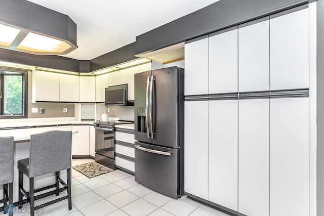 kitchen featuring white cabinetry, a breakfast bar area, light tile patterned floors, and stainless steel appliances