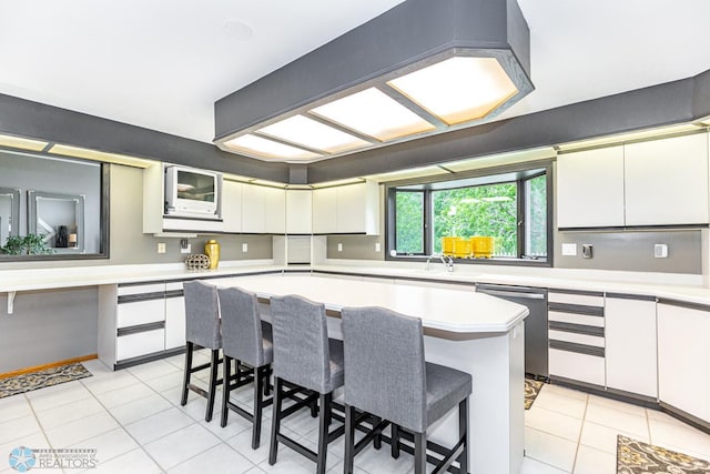 kitchen featuring a breakfast bar area, white cabinetry, light tile patterned floors, dishwasher, and a kitchen island