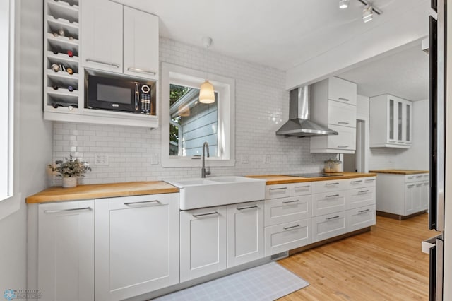 kitchen featuring black appliances, wooden counters, wall chimney range hood, white cabinets, and light hardwood / wood-style floors