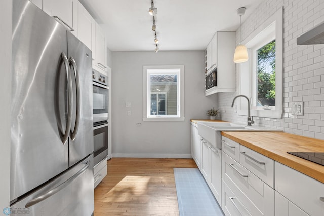 kitchen featuring white cabinets, black appliances, hanging light fixtures, and light wood-type flooring