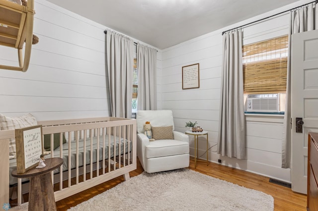 bedroom with light hardwood / wood-style flooring, a crib, and cooling unit