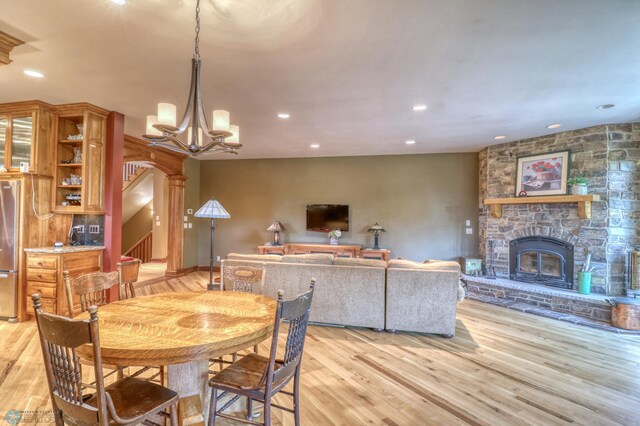 dining area with an inviting chandelier, a fireplace, and light wood-type flooring