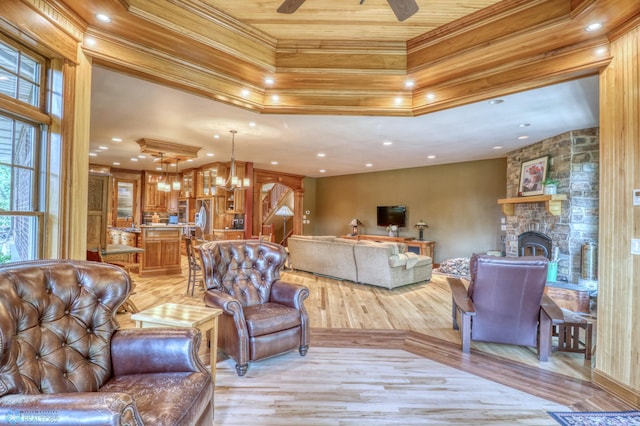 living room featuring a fireplace, ceiling fan with notable chandelier, light wood-type flooring, and a tray ceiling