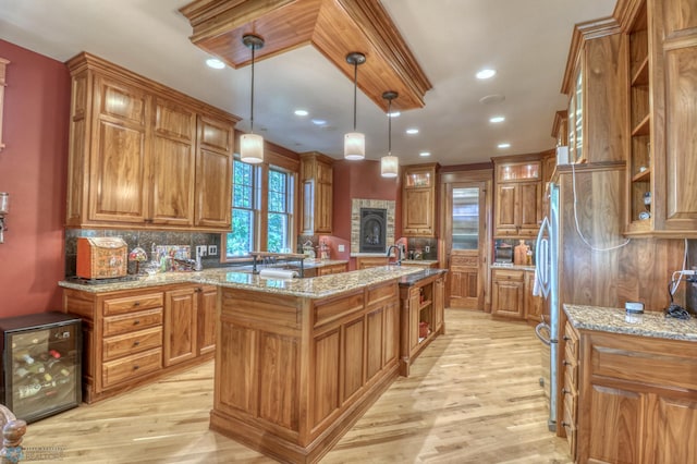 kitchen with pendant lighting, light stone countertops, wine cooler, light hardwood / wood-style floors, and a kitchen island with sink