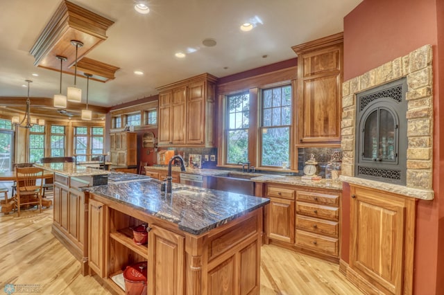 kitchen featuring dark stone countertops, a fireplace, light hardwood / wood-style floors, and an island with sink