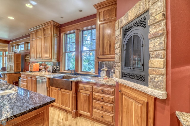 kitchen featuring tasteful backsplash, light wood-type flooring, dishwasher, stone countertops, and sink