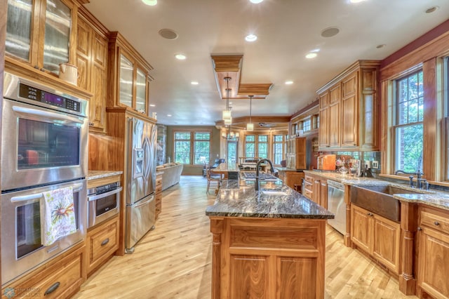 kitchen featuring dark stone countertops, light hardwood / wood-style flooring, appliances with stainless steel finishes, and a center island with sink