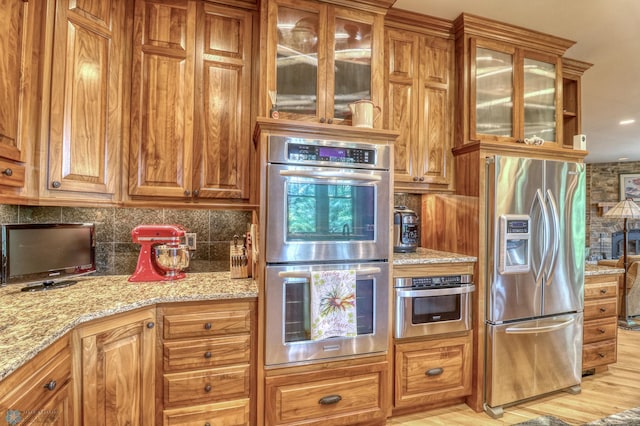 kitchen featuring light hardwood / wood-style floors, light stone countertops, decorative backsplash, and stainless steel appliances