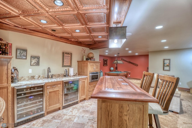 kitchen featuring light stone counters, beverage cooler, stainless steel oven, and light tile patterned floors