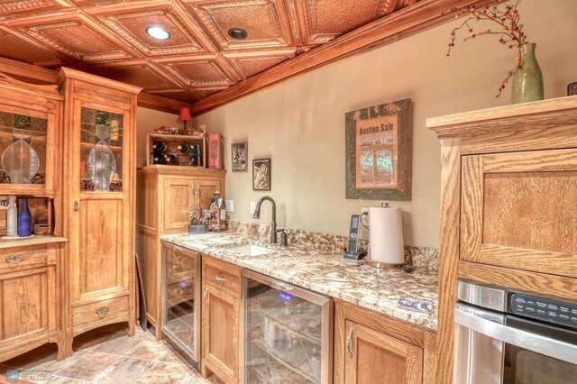 kitchen with sink, light stone counters, oven, beverage cooler, and coffered ceiling