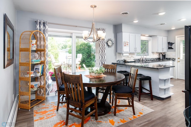 dining room featuring sink, a baseboard radiator, light wood-type flooring, and an inviting chandelier