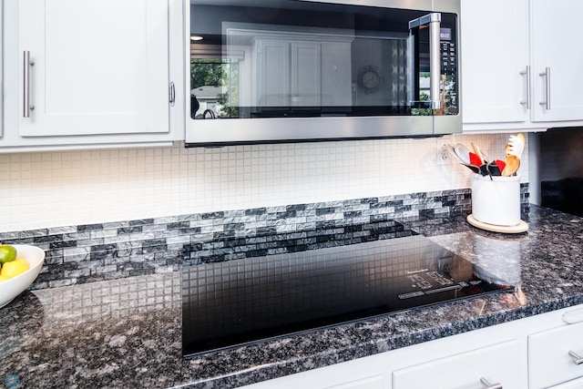 room details with decorative backsplash, white cabinetry, black cooktop, and dark stone counters