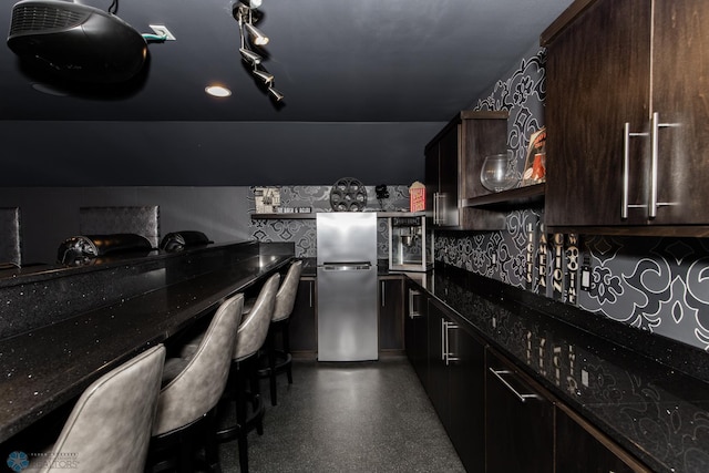 kitchen with dark stone countertops, decorative backsplash, refrigerator, and dark brown cabinetry