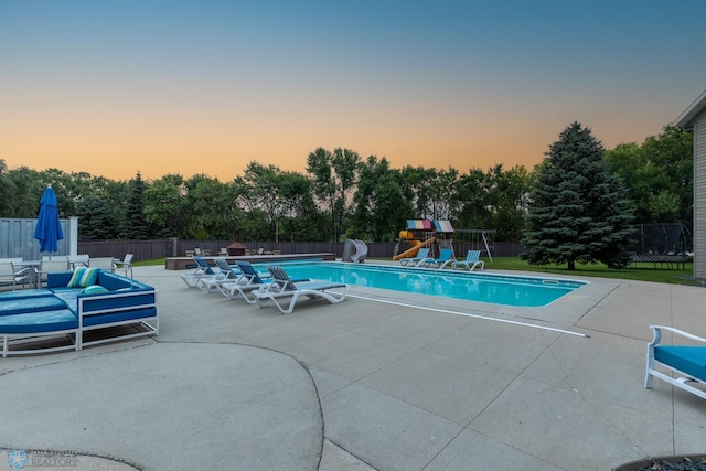 pool at dusk with a patio and a playground