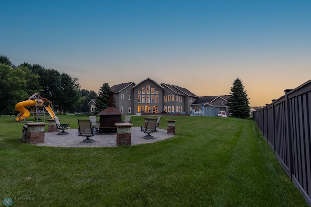 back house at dusk featuring a playground, a patio, and a yard