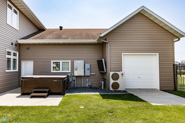 back of house with a garage, a lawn, and a hot tub