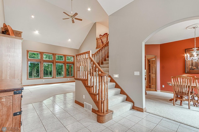 stairway with ceiling fan with notable chandelier, light colored carpet, and high vaulted ceiling