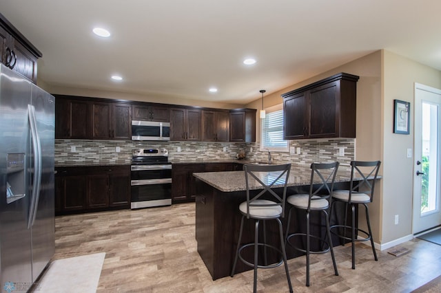 kitchen with tasteful backsplash, light wood-type flooring, appliances with stainless steel finishes, pendant lighting, and a kitchen breakfast bar