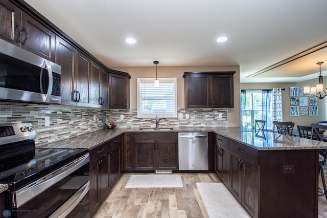 kitchen featuring light hardwood / wood-style flooring, hanging light fixtures, appliances with stainless steel finishes, decorative backsplash, and a kitchen breakfast bar