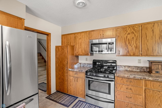 kitchen with appliances with stainless steel finishes, light tile patterned flooring, stone countertops, and a textured ceiling