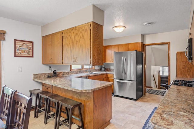 kitchen featuring appliances with stainless steel finishes, sink, kitchen peninsula, a kitchen breakfast bar, and light tile patterned flooring