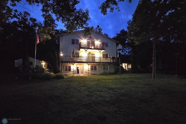 back house at twilight featuring a yard and a balcony