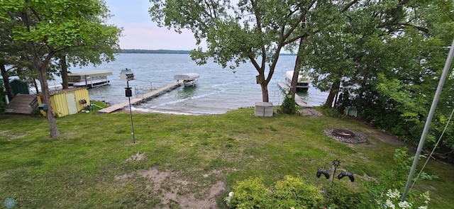 dock area with a water view, a lawn, and a fire pit