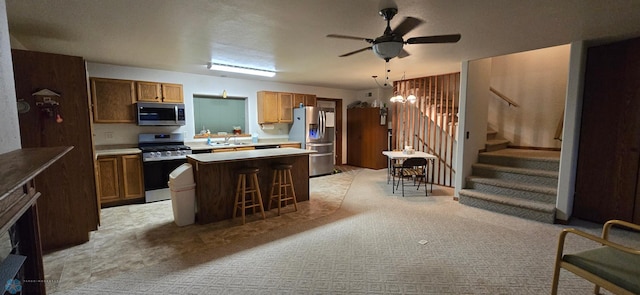 kitchen featuring a center island, ceiling fan, stainless steel appliances, light carpet, and a kitchen bar