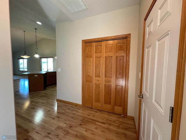 hallway featuring lofted ceiling, wood-type flooring, and a textured ceiling