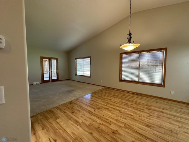 unfurnished living room with french doors, light colored carpet, and high vaulted ceiling