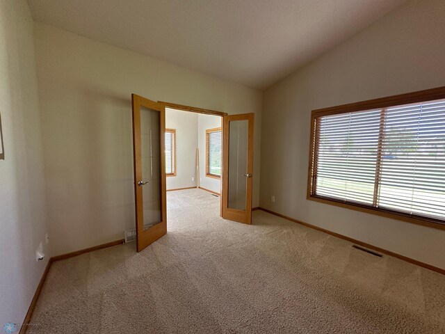 carpeted spare room with french doors and lofted ceiling