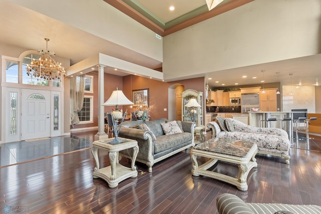 living room featuring ornate columns, an inviting chandelier, a towering ceiling, and dark hardwood / wood-style floors