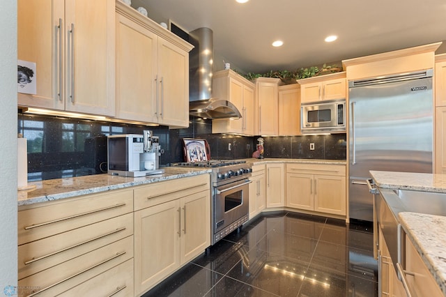 kitchen featuring light stone counters, built in appliances, wall chimney exhaust hood, and decorative backsplash