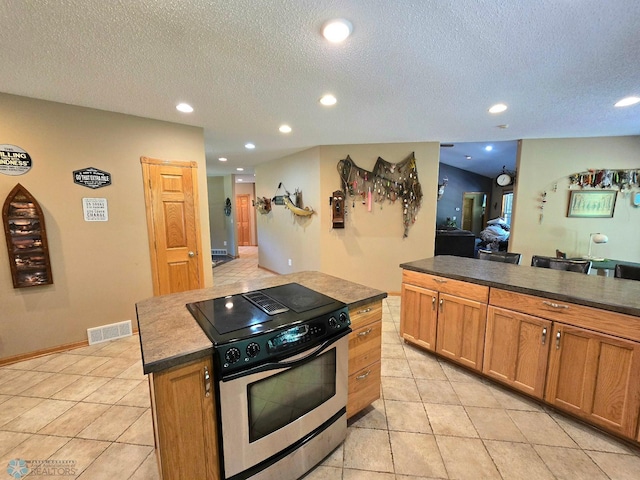 kitchen with stainless steel stove, a center island, a textured ceiling, and light tile patterned floors