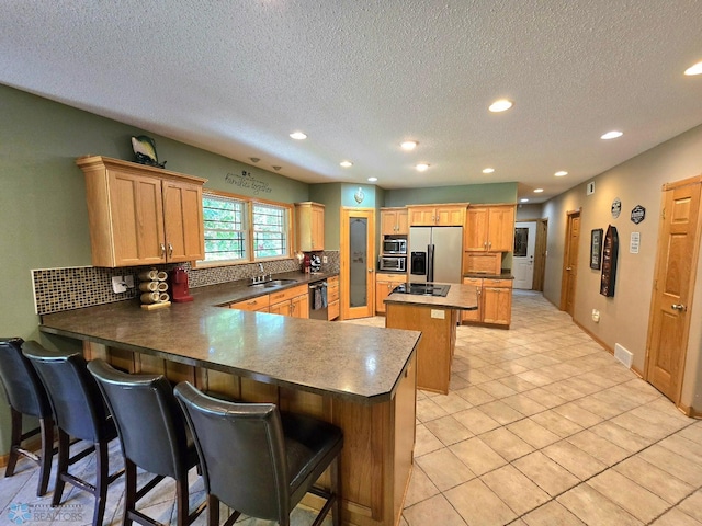 kitchen featuring appliances with stainless steel finishes, kitchen peninsula, light tile patterned floors, a kitchen breakfast bar, and a center island