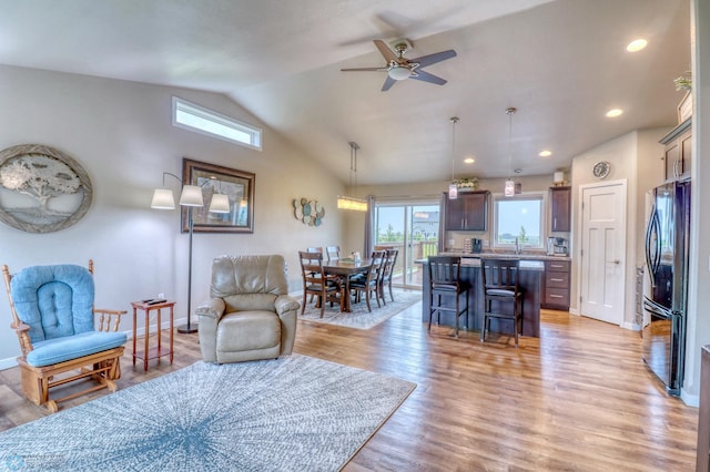 living room with light hardwood / wood-style floors, vaulted ceiling, sink, and ceiling fan