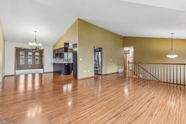 unfurnished living room with hardwood / wood-style flooring, an inviting chandelier, and high vaulted ceiling