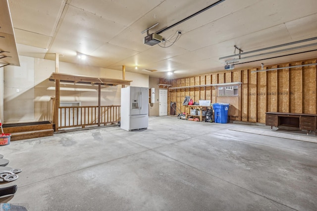 garage with a garage door opener and white refrigerator with ice dispenser