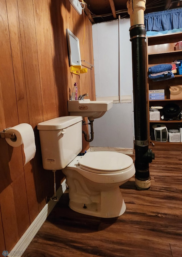 bathroom with wood-type flooring, sink, wooden walls, and toilet