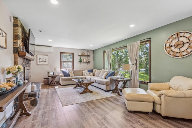 living room with a fireplace, a wall mounted AC, hardwood / wood-style flooring, and a wealth of natural light